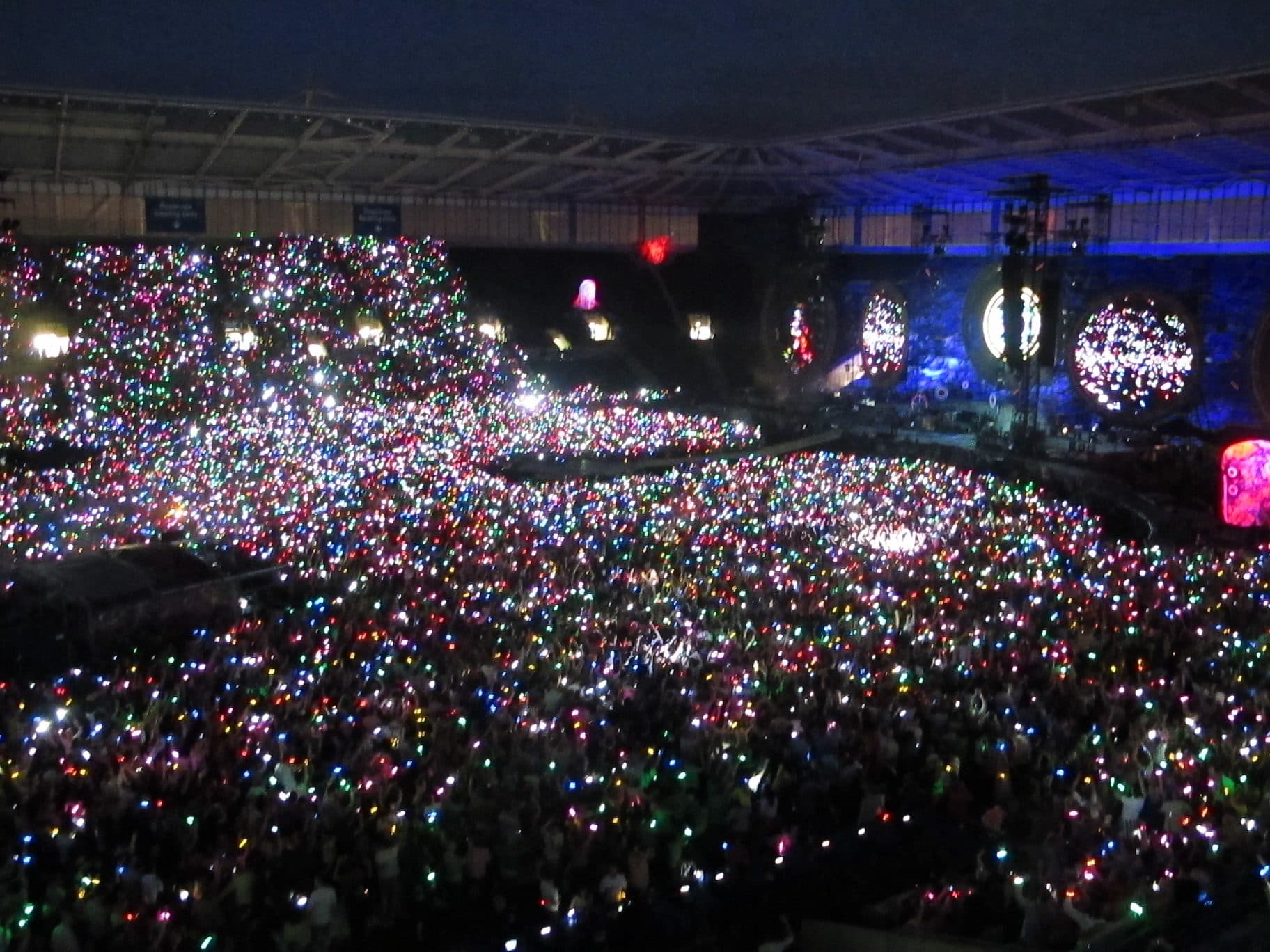 A stadium crowd at night wearing LED xylobands, thousands of wristbands lit in colour across the stands